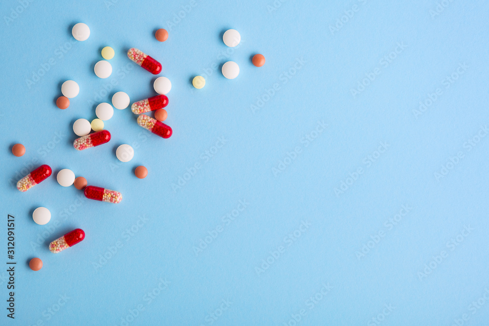 Heap of pills and capsules spilling on blue background. Medicine concept. Copy space. Heap of pills and capsules spilling on blue background. Medicine concept. Copy space.