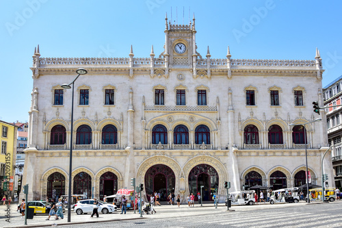 Lisbon, Portugal - Rocio Station (Rossio Train Station), a beautiful white building with horseshoe-shaped doors and a clock at the top, a street with cars and people in the summer afternoon. © Ivars