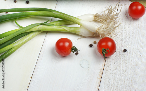 A sprig of green onion and three cherry tomatoes lie on a white wooden table