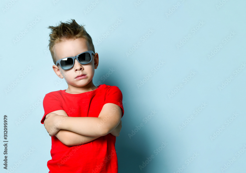 Serious boy in bright stylish casual clothing and sunglasses standing over blue background Serious boy in bright stylish casual clothing and sunglasses standing over blue background