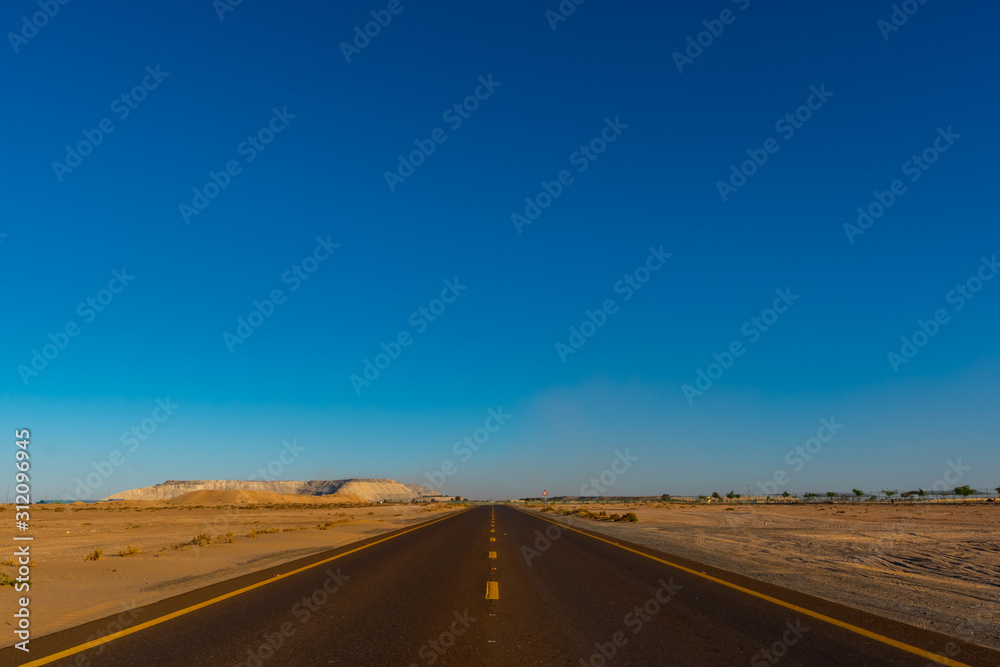 View from the center of the road to infinity in the deserted area with blue sky. Shot at summer day time. Vacation travel. 