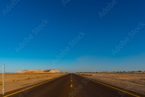 View from the center of the road to infinity in the deserted area with blue sky. Shot at summer day time. Vacation travel. 