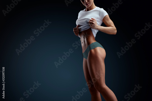 Close up of fit woman's torso with her hands on t-shirt. Woman bodybuilder resting after workout. Horizontal studio shot with copy space on black background.