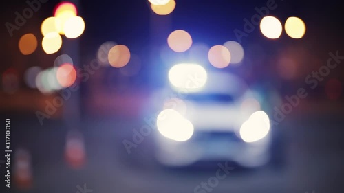 Unfocused shot, front view of police car and officer at night. Road traffic accident concept. Street lamp lights bokeh.