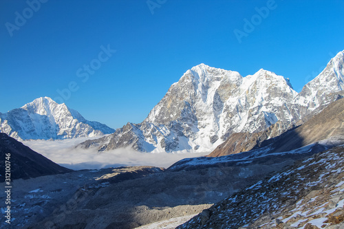 Taboche and Kangtega mountain peaks rises above Khumbu glacier and valley covered with clouds in the early morning in Himalayas. Theme of trekking in Nepal. Clear blue sky.
