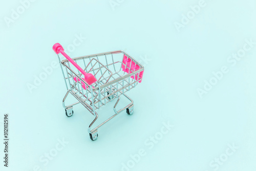 Small supermarket grocery push cart for shopping toy with wheels isolated on blue pastel colorful trendy background Copy space. Sale buy mall market shop consumer concept.