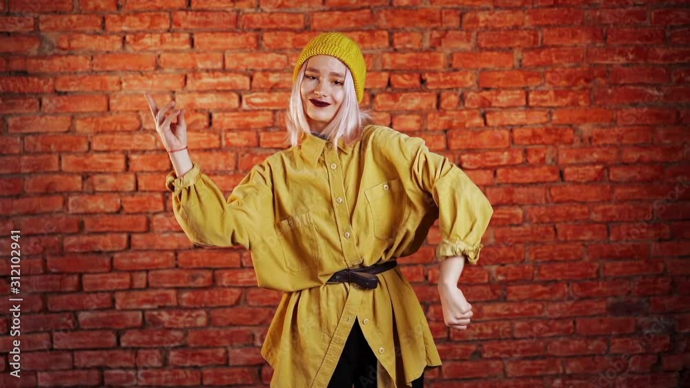 Unusual woman with pink hair having fun, smiling, dancing in studio against bricks background. Music, dance concept, slow motion