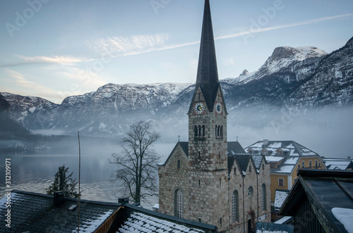 The cathedral of Hallstatt and the foggy mountains behind in Winter
