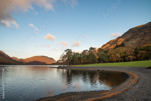Majestic vibrant Autumn Fall landscape Buttermere in Lake District with beautiful early morning sunlight playing across the hills and mountains