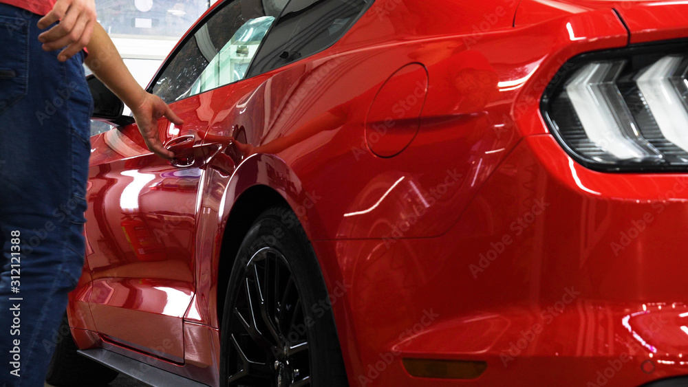 Fototapeta premium A man in the garage (car service) Checks the red sport car alarm and then goes off (comes in) turning off (turning on) the lights behind him. Concept of: Auto garage, Security. 