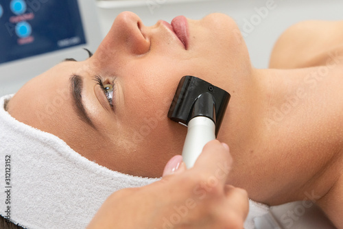 Młoda kobieta, zbliżenie na twarz podczas zabiegu specjalistycznym urządzeniem w salonie urody. Kuracja przeciwzmarszczkowa. 