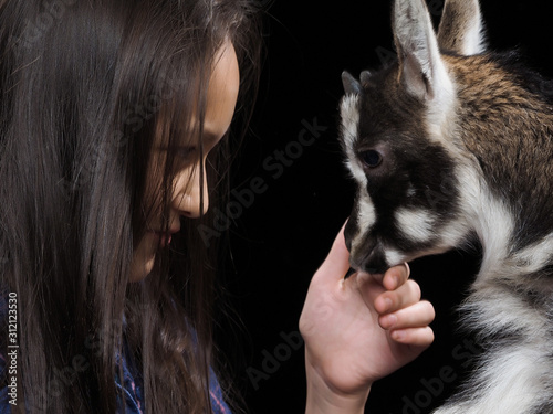 Portrait of a girl with a small goat on a black background