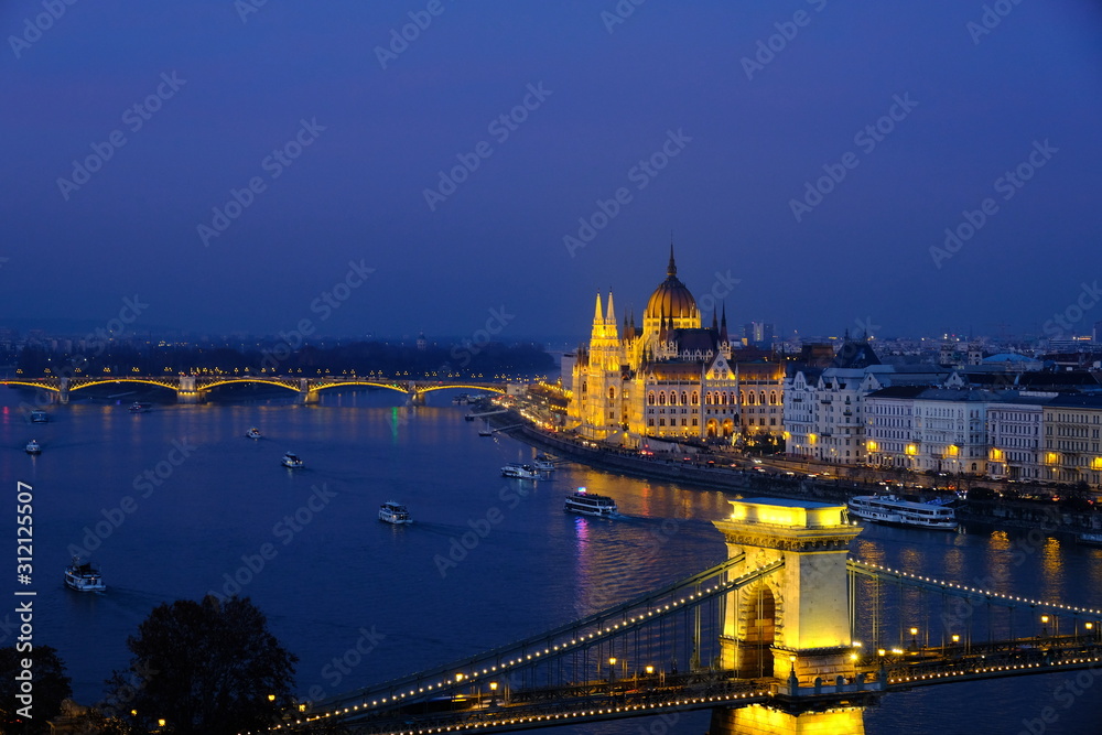Panoramic view of Budapest at night. Illuminated Hungarian Parliament Building on Danube river and Széchenyi Chain bridge.