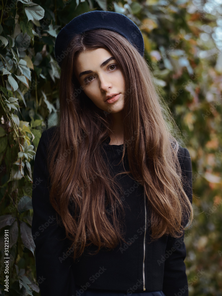 Naklejka premium Mood contrasty portrait young elegant french style brown haired woman in beret and black leather jacket enjoying free time strolling in fall city park cinematic stock colour grading ivy background