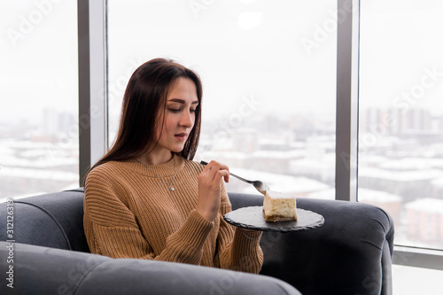 girl eating a cake while sitting in a chair in front of a large window on a winter day Free Download girl eating a cake while sitting in a chair in front of a large window on a winter day - GFXLoad