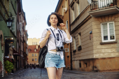 The girl in the black hat and sun glasses with photo camera on a road in an old european town.