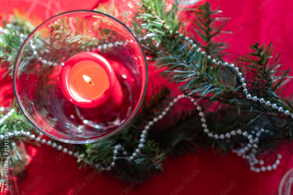 Table setup lunch in red for celebration. Shiny glass cup, red tablecloth, candles and decorations with green Christmas tree. Christmas dinner during the holiday decorated table. Dining table setup Table setup lunch in red for celebration. Shiny glass cup, red tablecloth, candles and decorations with green Christmas tree. Christmas dinner during the holiday decorated table. Dining table setup