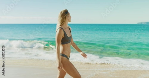 Young attractive healthy woman walking on a sunny tropical beach, happy smiling woman enjoying the beach on vacation