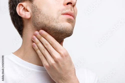 Close up of sick man suffering from throat problems, grey background, isolated. Lymph glands, painful swallowing, pharyngitis, laryngeal swelling concept. Inflammation of the upper respiratory tract photo