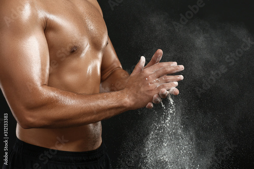 Sporty African-American man applying talc powder on hands against dark background  closeup