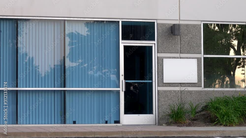 A generic office building glass front door and windows with vertical blinds are shown from the exterior during the day.