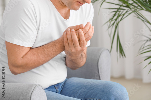 Mature man suffering from pain in wrist at home