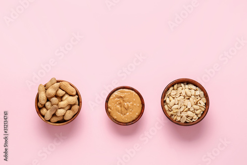 Bowls with peanut butter and nuts on color background