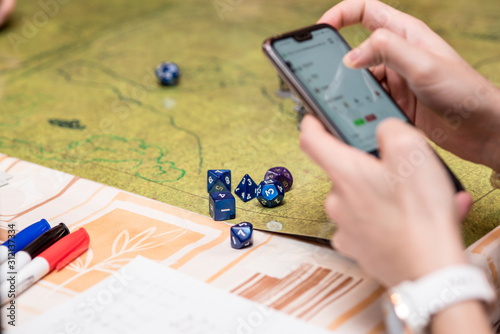 Girl using the smartphone during a role-playing game of dungeons and dragons. Dices on the green battlefield