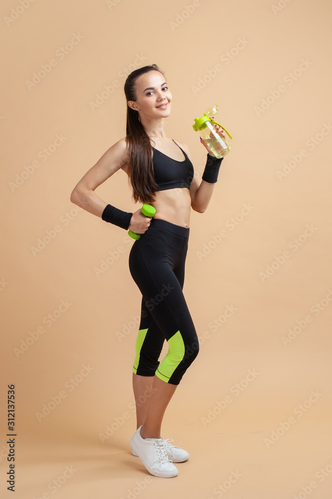 An attractive athletic girl, with a tight-fitting athletic uniform, stands  tall, drinks water from bottle after workout. Stock Photo