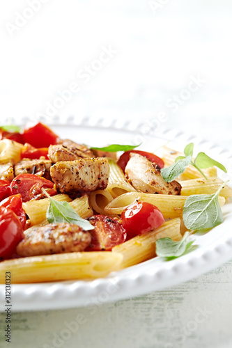 Penne pasta with cherry tomatoes, chicken breast and fresh basil. Bright wooden backgroudn. Close up. 