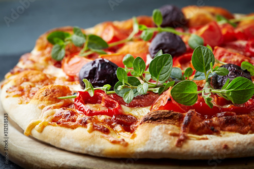 Pizza with mozzarella cheese, cherry tomatoes, black olives and fresh oregano. Home made food. Concept for a tasty and hearty meal. Black stone background. Close up. 