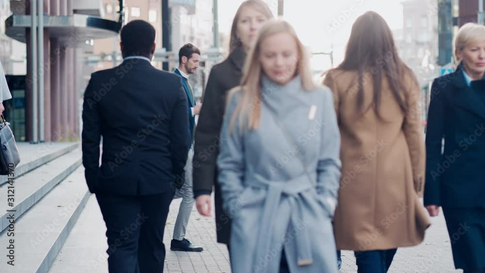 Diverse and Multicultural Office Managers and Business People Commute to Work in the Morning or from Office on a Cloudy Day on Foot. Pedestrians are Smart Casually Dressed. People Using Smartphones. Diverse and Multicultural Office Managers and Business People Commute to Work in the Morning or from Office on a Cloudy Day on Foot. Pedestrians are Smart Casually Dressed. People Using Smartphones.