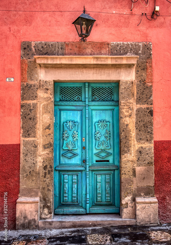 A beautifully restored vintage door painted turquoise with a stone frame and red wall