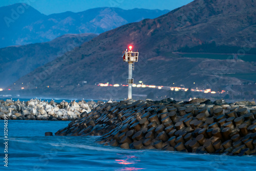 Ventura harbor mouth rock jetty wet from rising tidal swell with freeway headlights in the distance. © motionshooter