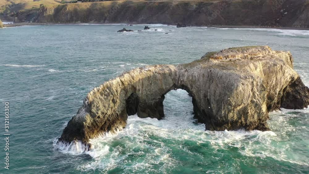 The cold waters of the Pacific Ocean wash around a massive natural arch ...
