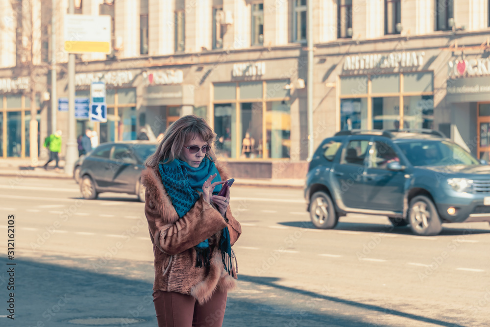 Obraz premium A woman with a smartphone in hands stands on a city street