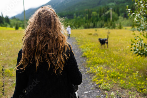 back view of a young jogging girl in the woods on a dirt road with her dog on a leash with forest and mountain 