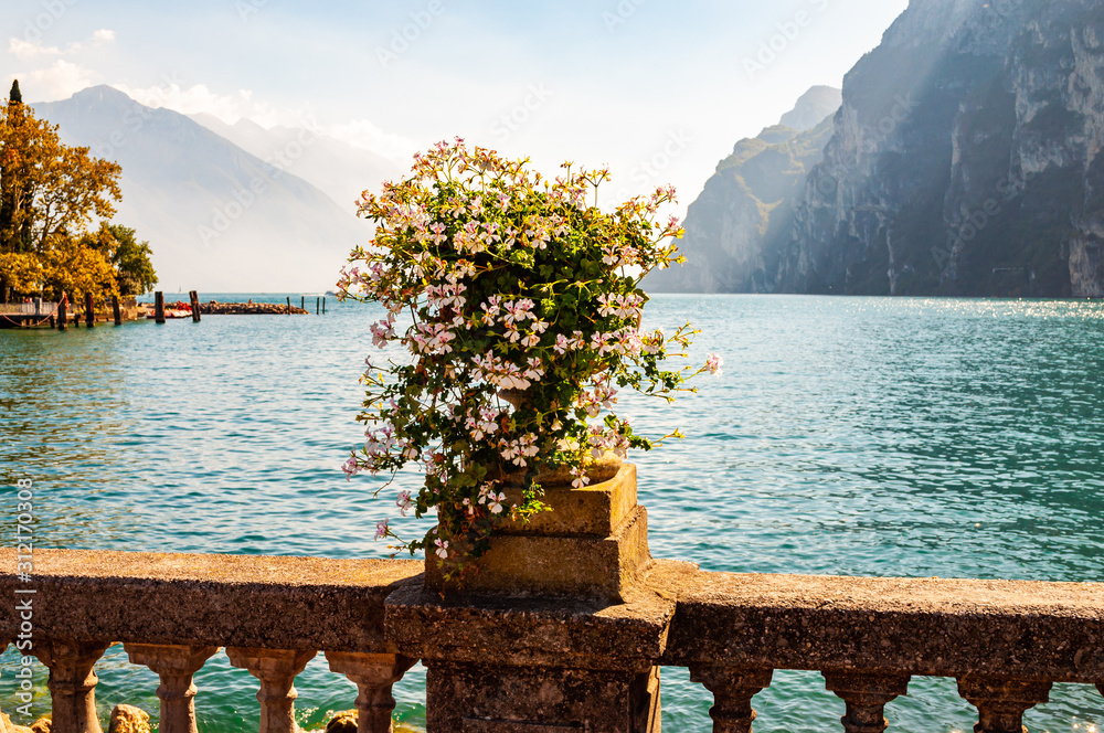 Φωτογραφία Beautiful Garda lake promenade with classic stone fence railings built on the edge with flowerpots with blooming white flowers
