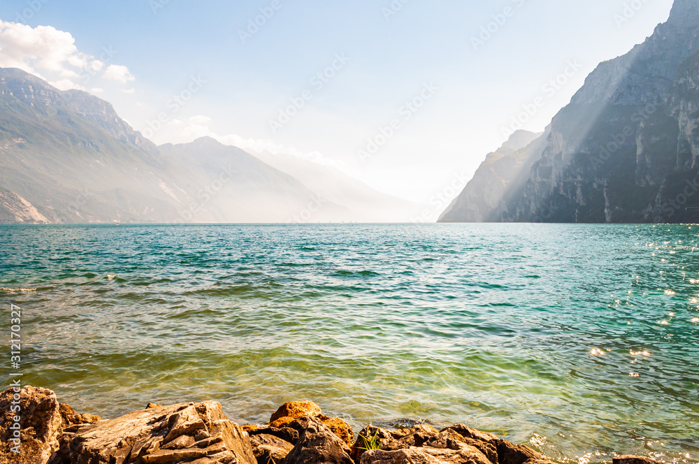 Φωτογραφία Rocky stones lying on the shore of beautiful Garda lake in Lombardy, Italy surrounded by high dolomite mountains