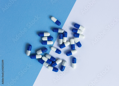 Blue and white medical capsules are piled high on a blue background. photo