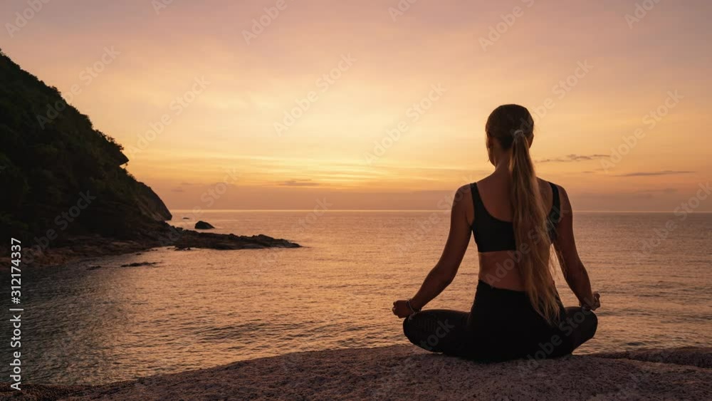 Young woman sitting and meditating in lotus position on a rock by the sea against the background of sunset . 4k time lapse Young woman sitting and meditating in lotus position on a rock by the sea against the background of sunset . 4k time lapse