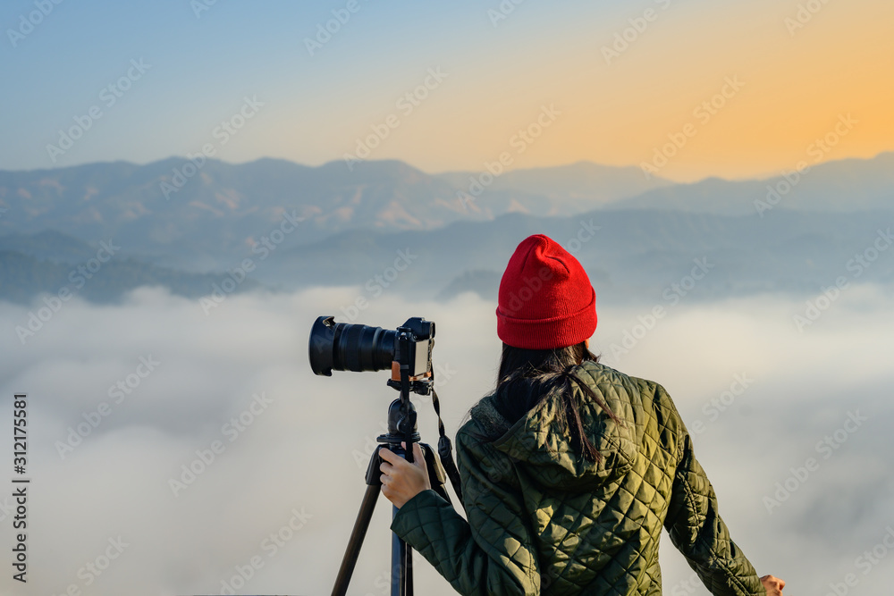 young woman traveller, photographer in the top peak of mountain in jungle forest alone, enjoy taking nature photo of the mist and flowing of foggy, northern part of Thailand travel