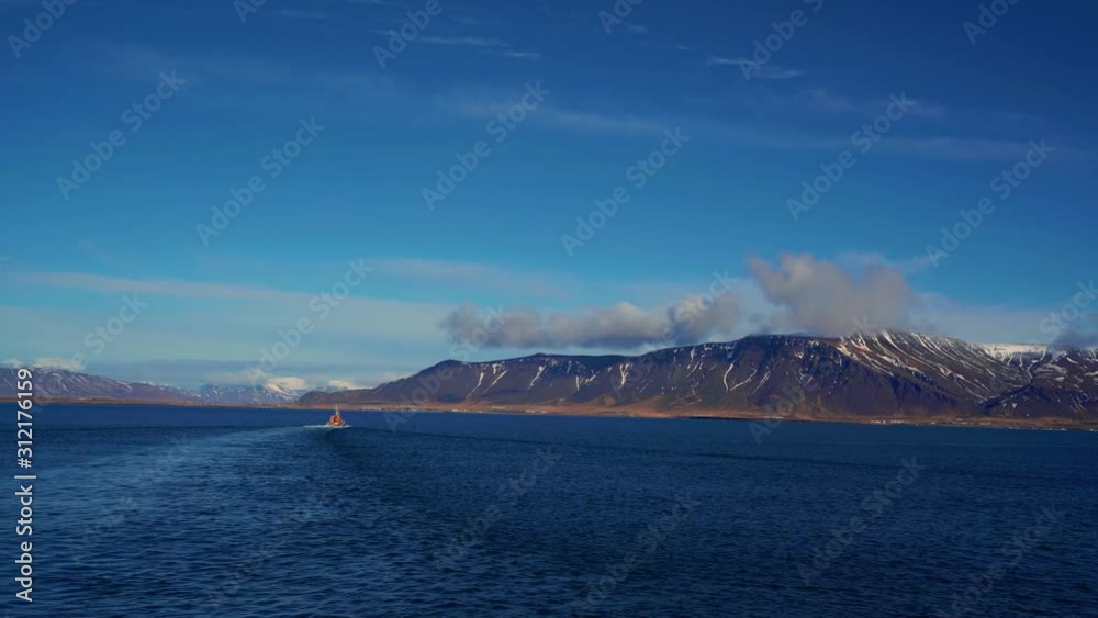 View of a landscape from the Reykjavik bay from a moving boat. A whale watching boat in a distance. View of a landscape from the Reykjavik bay from a moving boat. A whale watching boat in a distance.