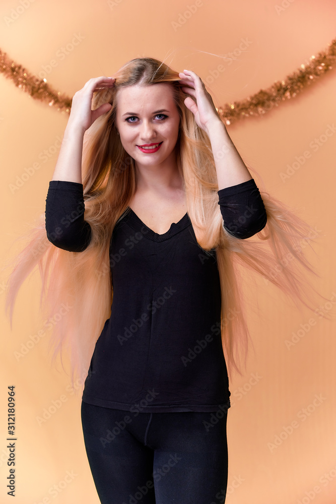 Obraz premium Portrait of a cute girl in a black T-shirt with long beautiful hair and great makeup. Concept of a young blonde woman with New Year's decor. Smiling, showing emotions on a pink background.