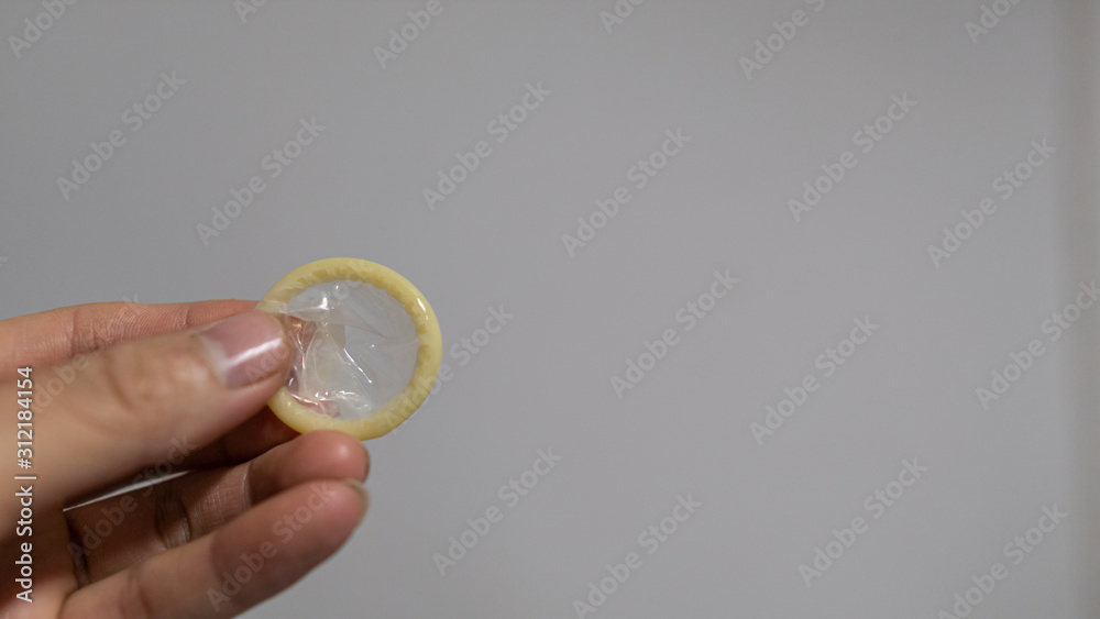 A man with a condom in his hand, gray wall background