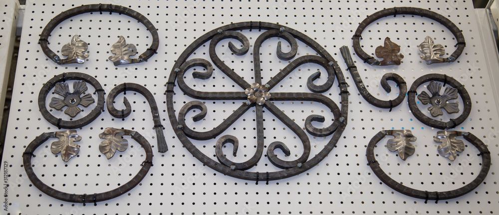 Forged metal products in the form of curls, circles, flowers, leaves fixed on a white stand. Construction, repair, art,  design.