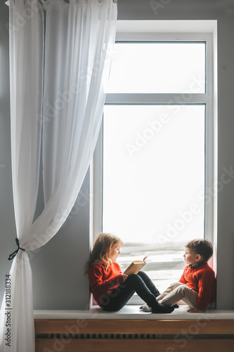 Cute little girl reading book for her two year old brother.
