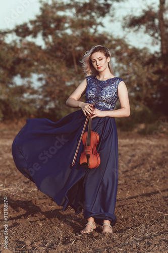 face of a beautiful girl with a violin under her chin outdoors, young woman playing a musical instrument on nature in solitude, concept music and feelings
