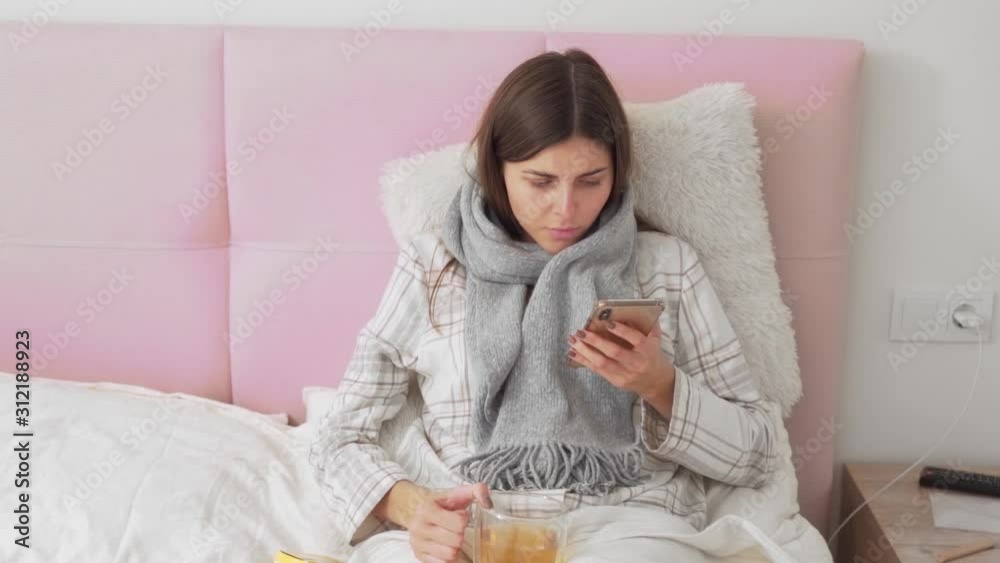 sick girl lying in bed reading on the phone about pills and drinking tea sick girl lying in bed reading on the phone about pills and drinking tea