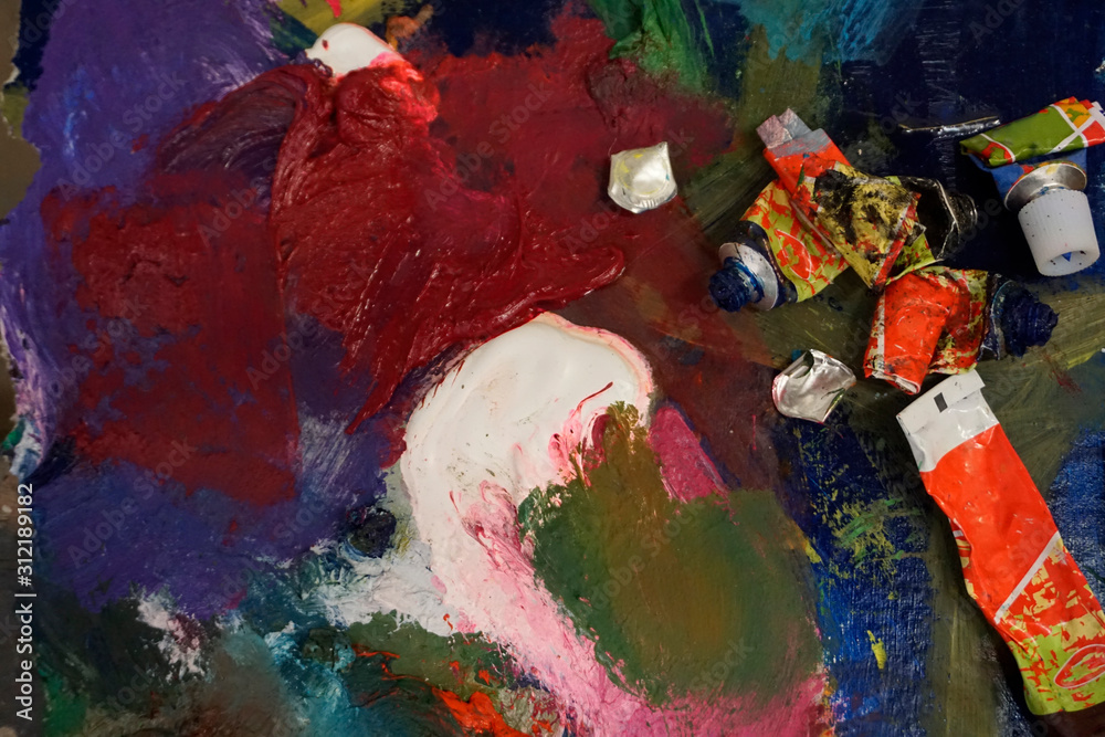 Obraz premium Artist's palette with oil paints and brushes, soft focus. Artistic paintbrushes, paints and palette knife on an old wooden palette, view from above.